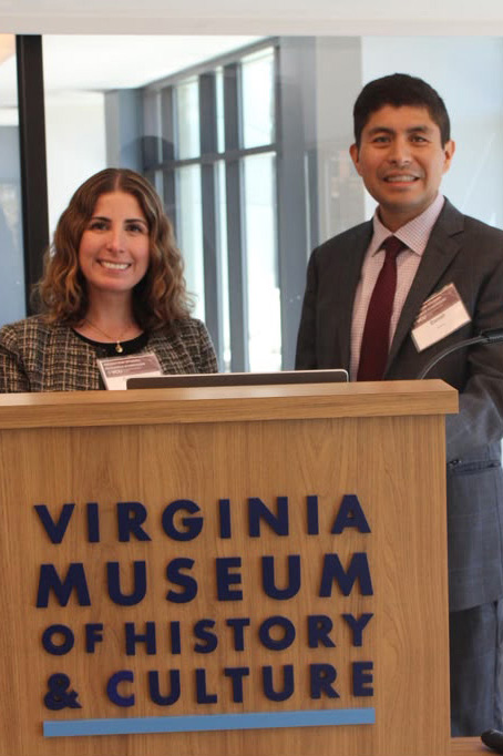 Professors Gabriela Leon-Perez and Daniel Morales stand at a podium with lettering that reads Virginia Museum of History and Culture